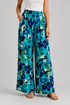 Pantalon large femme à imprimé floral bleu turquoise porté avec débardeur blanc sur fond gris-VUE DE FACE
